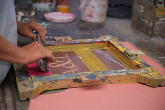 Lahore, Pakistan - 02 October 2024: View of a worker using a squeegee for screen printing on a fabric surface in a workshop at Quaid-e-Azam Industrial Estate.