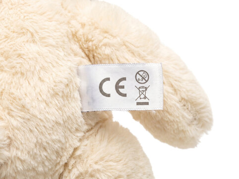Close-up of a soft plush toy tag with CE safety certification mark on beige fabric on transparent background