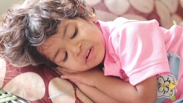 Close-up b-roll footage of a cute Indian toddler girl with curly hair peacefully taking a nap, slowly opening her eyes, and falling back asleep in soft natural sunlight.
