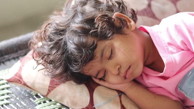 Close-up b-roll footage of a cute Indian toddler girl with curly hair peacefully taking a nap, slowly opening her eyes, and falling back asleep in soft natural sunlight.
