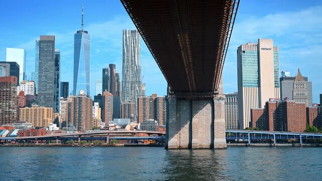 New York, USA, 4 Jule 2026 : Brooklyn Bridge underside framing Manhattan skyline. One World Trade Center rises above the East River beyond the bridge stone pier and steel girders.