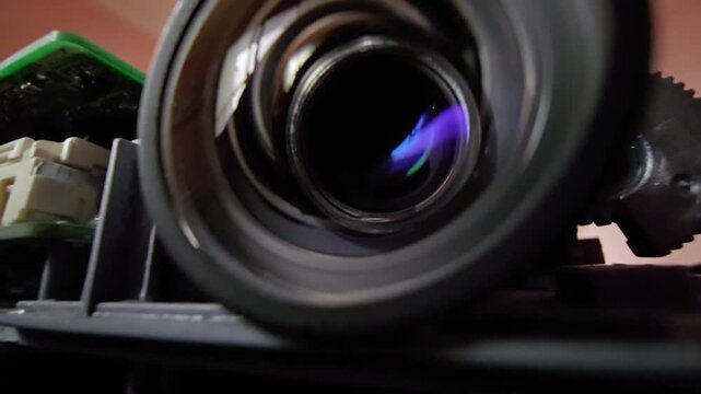 Extreme macro close-up shot focusing on an optical camera lens element with purple lens flare and visible circuit board components. Ideal for technology, engineering, hardware, and cinematic concept v