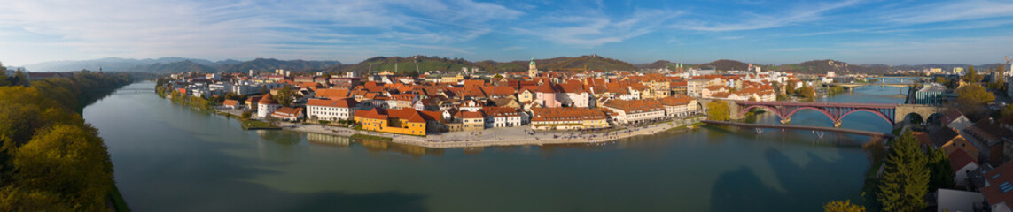 Fototapeta premium Aerial panoramic view of Maribor, Slovenia, with the historic old town, Drava River, Old Bridge, riverside promenade and surrounding hills.