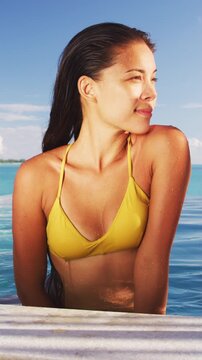 Luxury swimming pool Asian bikini model woman wearing yellow fashion swimsuit relaxing in pool at vacation travel resort. Raw unedited vertical video of real unretouched woman model without makeup