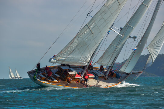 Ilhabela, Sao Paulo, Brazil - 03 September 2026: View of a classic wooden sailboat heeling over in the water with crew members on deck and white sails full of wind.