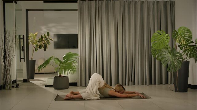 female yoga practitioner in downward dog pose in indoor studio with curtains and plants. side viewc.