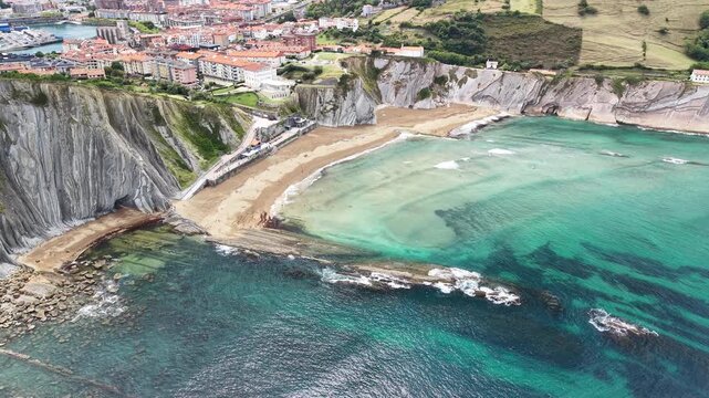 Cinematic aerial drone footage flying backward away from the majestic vertical flysch rock strata of Itzurun Beach out towards the vast open waters of the Atlantic Ocean, Spain &ndash; 2026