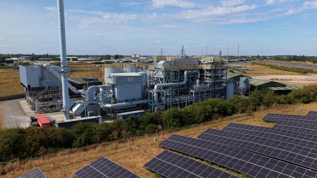 Aerial view of the Biomass Nr. 3 Energy Recovery Facility with rows of solar panels in the foreground, industrial pipes, and a tall chimney in Boston, England, United Kingdom.