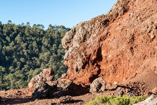 Weathered volcanic rock formation rises from red oxidized earth above a pine-forested valley in Cumbres del Ajusco National Park in Mexico City, Mexico