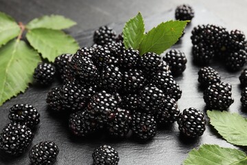 Pile of fresh blackberries and green leaves on dark textured table, closeup © New Africa