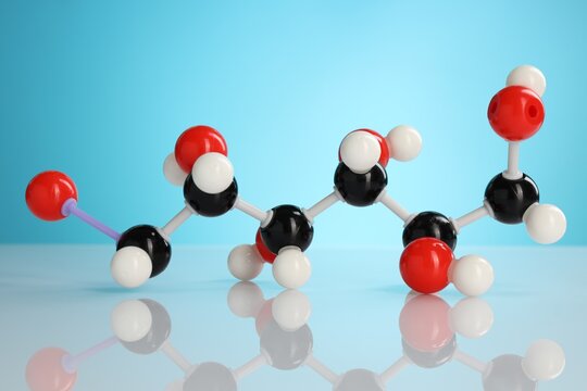 Chemical model of glucose molecule on white table against blue background, closeup