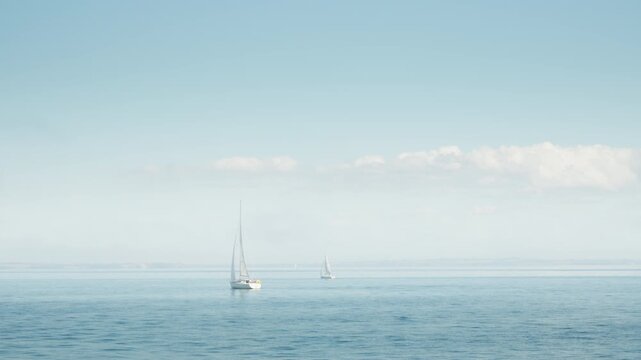 Sailboats cruise across calm open sea waters under a clear sky. Peaceful ocean sailing journey offers summer leisure travel, freedom, and tranquil horizon background for maritime navigation.