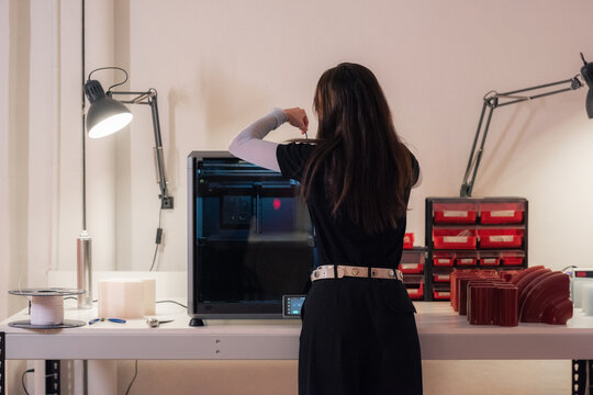 Woman preparing 3d printer for work at workshop