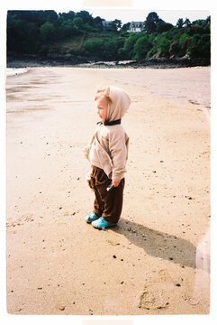 Child standing alone with a bucket of seashells on a sandy beach