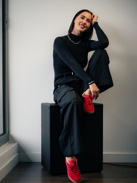 Woman Sitting on Guitar Amplifier With One Leg up and Smiling