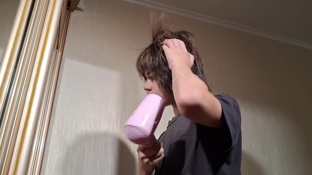 13 year old boy ties his hair in a room while preparing for an activity