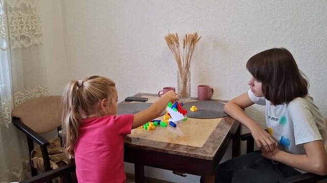 13 year old boy plays with a younger girl at a table in a home setting in the afternoon
