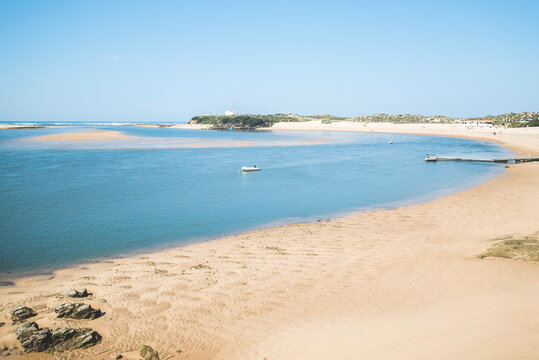 Mira River, Vila Nova de Milfontes, Portugal: Wide sandy beach and calm estuary with a small boat under blue sky