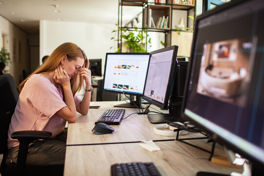 Stressed woman rubbing eyes at computer in modern office