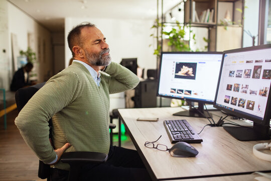 Mature office worker with neck pain at computer desk in modern office