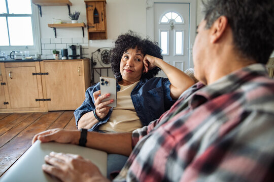 Mature couple discussing smartphone on living room sofa at home