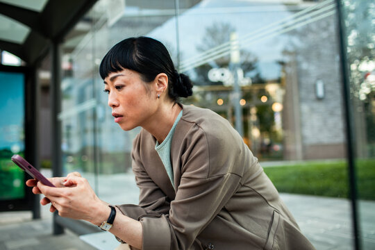 Woman using smartphone while waiting at city bus stop