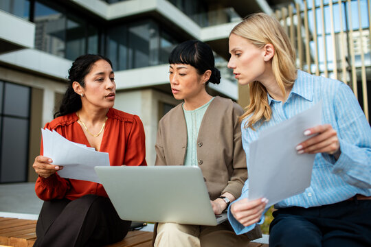 Three colleagues discussing documents with laptop outside office