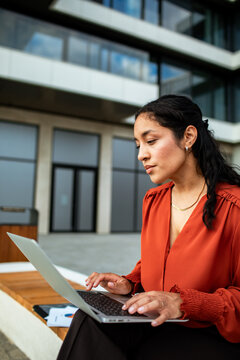 Confident businesswoman working on laptop outside modern office building