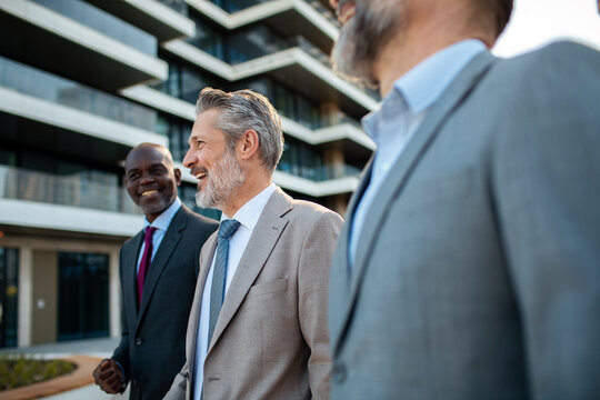 Three senior businessmen walking outside modern office building