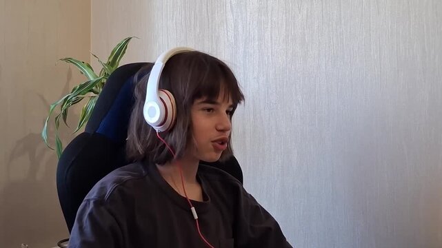 13 year old boy wearing headphones sits in a chair smiling and enjoying his time indoors