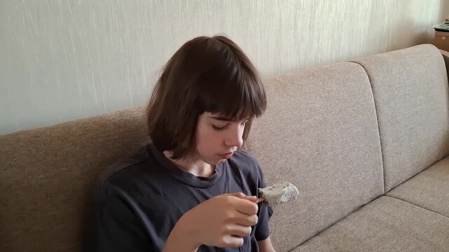 13 year old boy sits on a couch and enjoys ice cream at home
