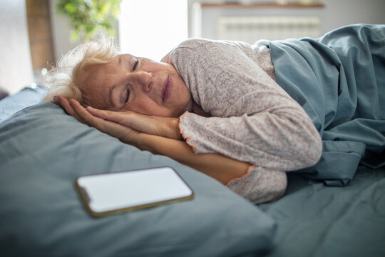 Senior woman sleeping in bed with smartphone at home
