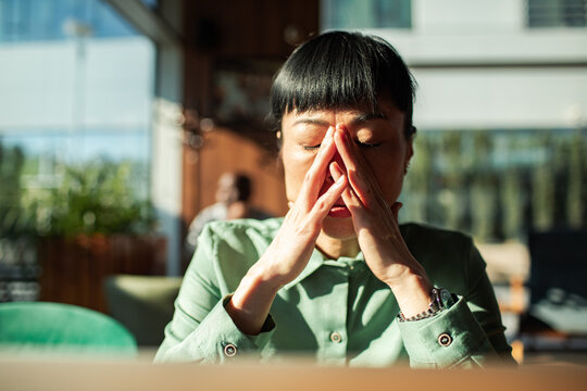 Stressed professional woman rubs face at sunlit cafe