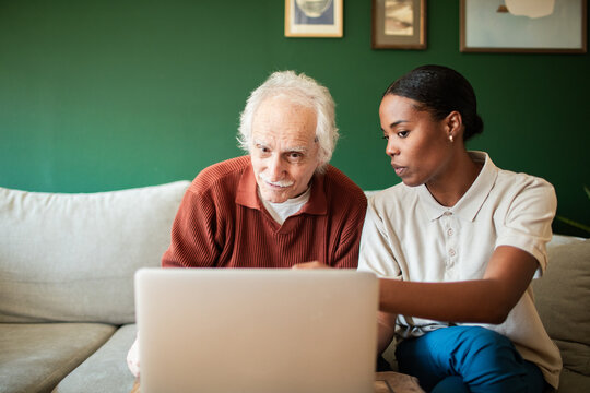 Caregiver helping senior man with laptop at home