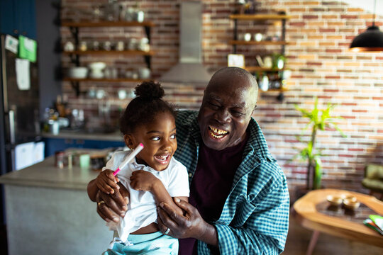 Grandfather hugging granddaughter with toothbrush in home kitchen