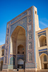 Historic madrasa architecture in Bukhara, Uzbekistan, featuring a monumental pointed iwan richly decorated with blue and turquoise mosaic tiles, geometric patterns, floral motifs © pploylp