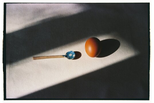 Brown egg and spoon  rests on light surface with shadows