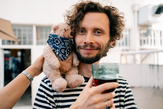 Man Holding Drink With Stuffed Bear on Shoulder at Outdoor Event