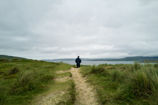 Man standing on sand dunes looking at the Ocean.
