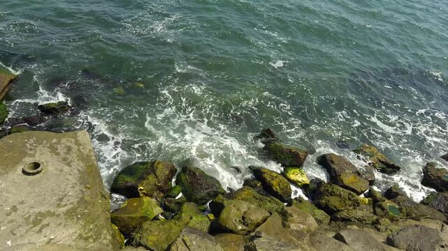 Sea Waves Crashing Against Mossy Coastal Rocks And Concrete Pier High. Sea Surf 