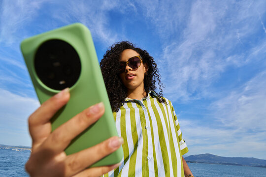 Woman holding smartphone taking selfie by the sea