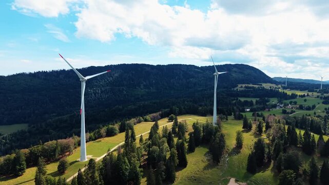 Aerial view of the Sainte-Croix wind farm with large wind turbines set against a backdrop of rolling green hills and forests in Sainte-Croix, Vaud, Switzerland.