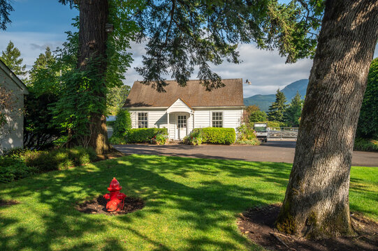 Cascade Locks, Oregon, United States - 16 August 2026: View of the white cottage at Bonneville Fish Hatchery with a red fire hydrant on the lawn and large trees.