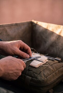Close up of military medic hands preparing surgical forceps and sterile gauze on a tactical first aid kit outdoors