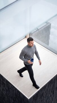 High angle view of a handsome mature businessman walking with coffee on a modern minimalist balcony