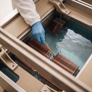 Cleanroom technician inspecting submerged copper heatsinks in an industrial ultrasonic cleaning liquid bath
