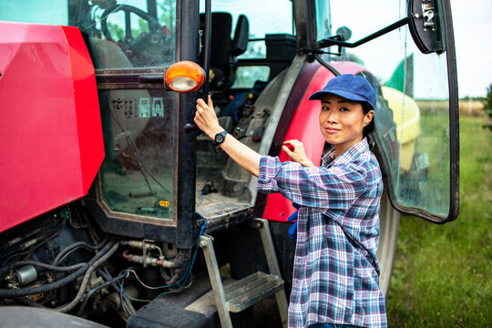 Female farmer opening red tractor door on farm