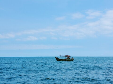 Small wooden fishing boat sailing on calm blue ocean under clear bright sky during peaceful summer day