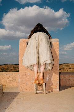 Person Climbing Rooftop Wall Against Cloudy Sky