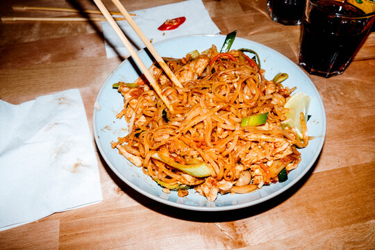a plate of chicken pad thai on a restaurant table with chopsticks